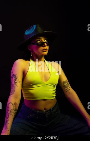 Une mannequin mexicaine regarde loin de l'appareil photo, portant un haut jaune fluo vibrant et un élégant chapeau noir. Elle est placée sur un fond sombre, haut Banque D'Images
