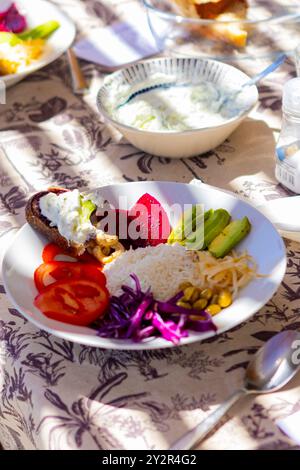 Une assiette vibrante de déjeuner végétalien servi dans une retraite axée sur la santé, avec betteraves, avocats, tomates, chou, maïs, et riz, niché dans la lumière du soleil o Banque D'Images