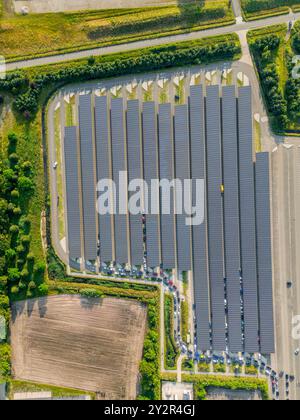 D’en haut, cette vue par drone met en valeur un vaste parc solaire aux côtés de parkings soigneusement organisés. Les différentes nuances de bleu des panneaux solaires c Banque D'Images