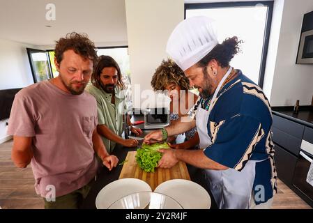 Groupe de quatre amis adultes dans une cuisine moderne, préparant joyeusement des légumes diverses expressions et implication, l'un d'eux avec un chapeau de chef et un Banque D'Images