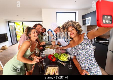 Groupe d'amis divers profitant d'un moment ensemble tout en se préparant pour un barbecue à l'intérieur Une joyeuse réunion avec du vin et de la nourriture, mettant en vedette un être selfie Banque D'Images