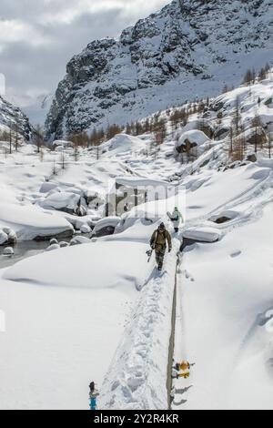 Randonneurs méconnaissables marchant le long d'un étroit chemin enneigé dans les Alpes suisses, près de Zermatt. Le paysage accidenté présente des rochers recouverts de neige et Banque D'Images