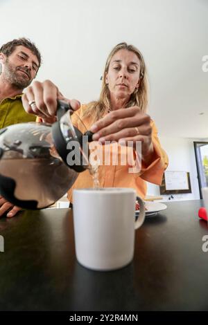Un homme et une femme sont engagés dans un début paisible de leur journée dans une cuisine moderne et bien éclairée. L'homme verse du café d'une presse française dans un blanc Banque D'Images