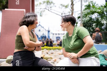 Un couple assis sur des rochers dans un parc s’engage dans une conversation animée, partageant un moment de rire. Les deux se regardent, affichant joyeux Banque D'Images