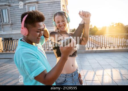 Deux heureux amis LGBTQIA+ dansent ensemble à l'extérieur, en profitant de la musique et d'un beau coucher de soleil. Ils partagent un moment de joie et d’amitié. Banque D'Images