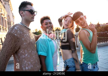 Un groupe d'amis LGBTQIA+ divers partagent des rires embrasser et danser devant un coucher de soleil urbain, rayonnant de positivité et de compagnie. Banque D'Images