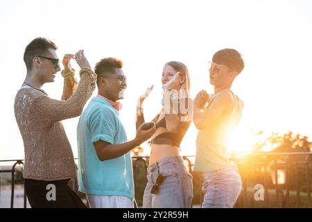 Un groupe d'amis LGBTQIA+ divers partagent des rires embrasser et danser devant un coucher de soleil urbain, rayonnant de positivité et de compagnie. Banque D'Images