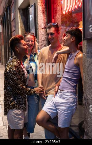 Un groupe diversifié d’amis LGBTQIA+ partagent des rires et de bons moments dans une rue animée de la ville la nuit Banque D'Images