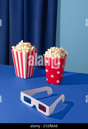 Image vibrante avec deux seaux à pop-corn et une paire de lunettes 3D sur un fond bleu profond, capturant l'essence de la soirée cinéma. Banque D'Images