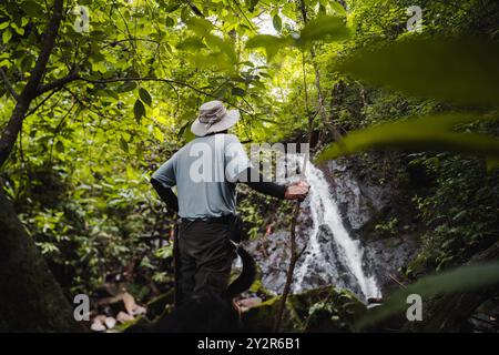 Un homme équipé d'un bâton marche à travers une forêt luxuriante et verdoyante vers une cascade au Costa Rica son voyage capture l'essence de l'aventu Banque D'Images