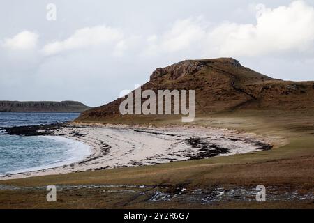 Une scène hivernale majestueuse dans les Highlands d'Écosse, avec une plage sereine bordée de falaises escarpées sous un ciel nuageux. Banque D'Images