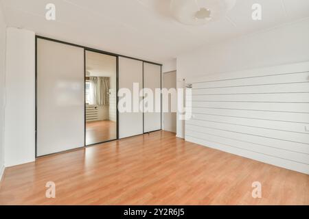 Spacieuse et lumineuse pièce vide avec de grandes portes de placard en miroir, un plancher en bois poli et des murs blancs, idéale pour les concepts de design d'intérieur. Banque D'Images