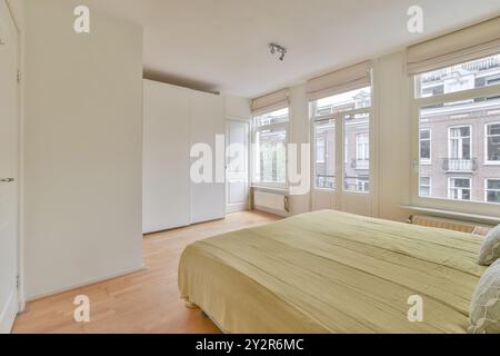 Une chambre confortable et bien éclairée avec un grand lit, du parquet, une armoire blanche et de larges fenêtres qui laissent entrer la lumière naturelle. Banque D'Images