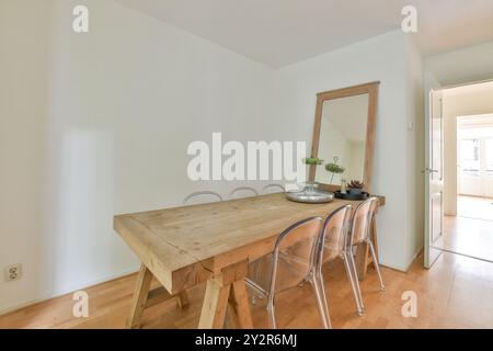 Un coin repas serein et minimaliste doté d''une table en bois rustique robuste, de chaises transparentes et d''un grand miroir. Banque D'Images