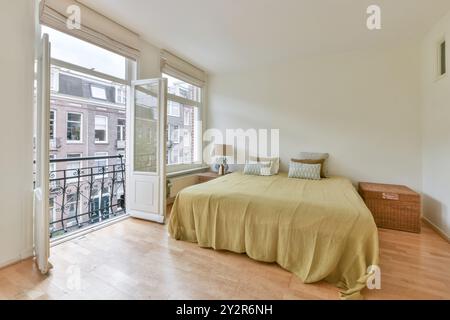 Une chambre confortable bien éclairée avec un grand lit avec des oreillers décoratifs, une double porte ouverte menant à un balcon avec balustrade en fer, et une vue sur le c Banque D'Images