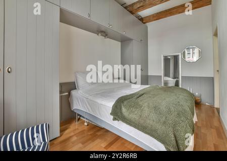 Cette chambre moderne dispose d''un lit confortable avec des draps blancs, d''une couverture verte, de poutres en bois et d''un rangement intégré. Banque D'Images