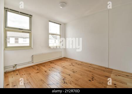 Cette chambre non meublée est dotée de parquet ciré, de murs blancs et de deux fenêtres baignant de lumière naturelle. Banque D'Images