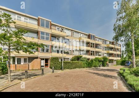 Immeuble résidentiel à plusieurs étages avec balcons, arbres et un ciel bleu clair par une journée ensoleillée. Banque D'Images