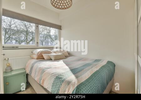 Cette chambre moderne bien éclairée dispose d''une grande fenêtre, d''un couvre-lit confortable à motifs et d''une table de chevet minimaliste. Banque D'Images