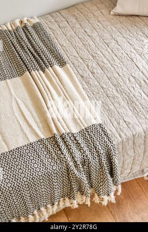 Une chambre chaleureuse et accueillante avec un lit soigneusement fait avec une couette texturée et un jeté décoratif. Banque D'Images