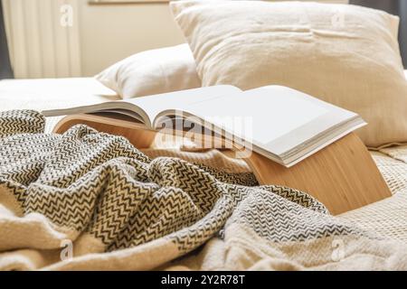 Un livre ouvert repose sur un support en bois, accompagné d'un jeté en tricot texturé, créant un espace de lecture tranquille. Banque D'Images