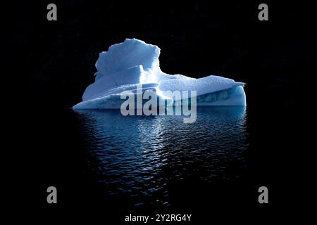 L'iceberg bleu flotte sur les eaux profondes du fjord de Dickson, dans le parc national du nord-est du Groenland. Fond sombre avec reflet montrant dans le ripp doux Banque D'Images