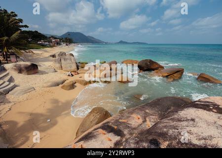 Une scène de plage pittoresque présente de grands rochers lisses le long du rivage, avec des vagues douces lançant sur la plage de sable sous un ciel bleu clair et SC Banque D'Images