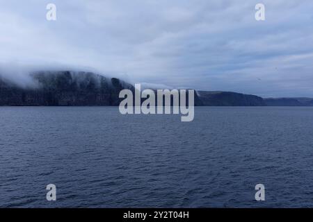 La plus grande falaise Látrabjarg oiseaux d'Europe le promontoire est vu du bord de l'eau en fin de soirée avec du brouillard roulant sur la falaise. Westfjords, Islande Banque D'Images