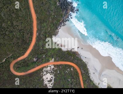 Vue aérienne d'un chemin de terre sinueux le long d'une plage côtière aux eaux turquoises et à la végétation luxuriante Banque D'Images