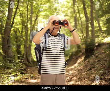 Randonneur mâle mature regardant à travers des jumelles dans une forêt Banque D'Images