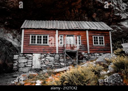 Une cabane en bois vieilli avec des fondations en pierre nichée contre les falaises rocheuses de Jossingfjord, Norvège. Banque D'Images
