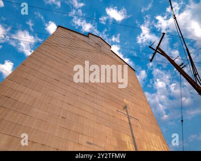 Les poteaux électriques projettent des ombres sur le mur en métal ondulé d'un vieil élévateur à grain tôt le matin Banque D'Images
