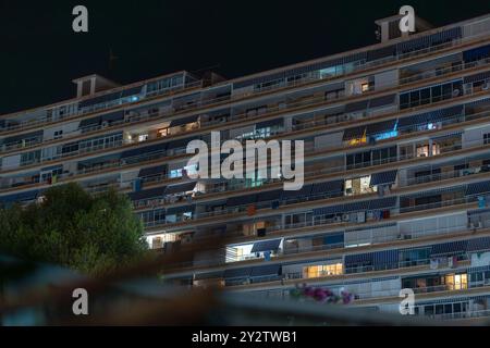 Une vue nocturne d'un immeuble résidentiel à Alicante, en Espagne, présentant des fenêtres et des balcons éclairés, créant un paysage urbain serein. Banque D'Images