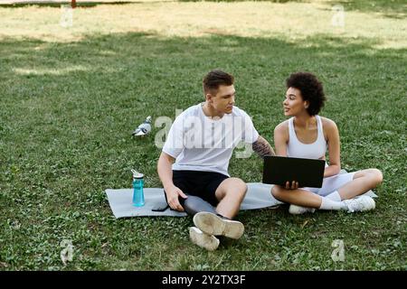 Deux amis s'engagent dans une séance d'entraînement amusante à l'extérieur, en utilisant un ordinateur portable sur l'herbe Banque D'Images