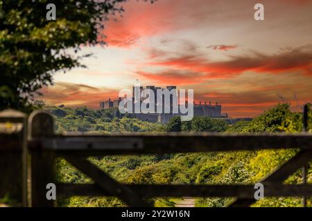 Une vue panoramique sur le château de Douvres au coucher du soleil, encadrée par une porte en bois et une végétation luxuriante. Banque D'Images