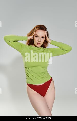 Une femme aux cheveux rouges saisissante pose gracieusement dans une mode chic et colorée. Banque D'Images