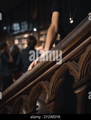 Gros plan de la main d'une femme reposant sur une balustrade d'escalier en bois à l'intérieur d'une bibliothèque faiblement éclairée Banque D'Images