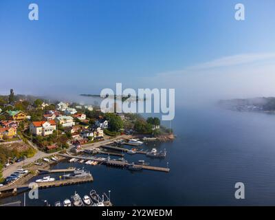 Brouillard matinal roulant sur une île au début de l'automne, Dalarö, archipel suédois, Suède. Maisons, arbres, bateaux. Ciel bleu, lumière du soleil éclatante Banque D'Images