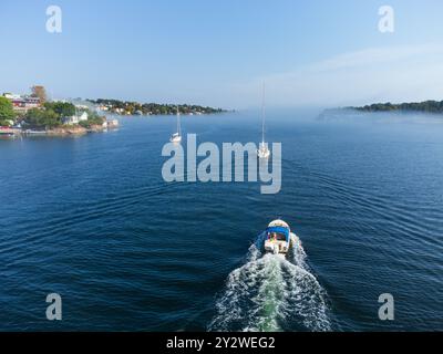 Voiliers et un bateau naviguant sur la mer avec le brouillard matinal roulant sur une île au début de l'automne, Dalarö, archipel suédois, Suède. Banque D'Images