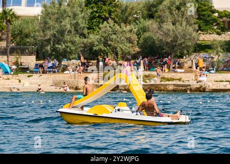 Porec, Istrie, Croatie - 27 août 2024 : la famille profite d'une balade en pédalo avec un toboggan au large de la côte de Porec, Croatie. Été, plaisir et détente au bord de la mer *** Familie genießt eine Fahrt im Tretboot mit Rutsche vor der Küste von Porec, Kroatien. Sommer, Spaß und Entspannung am Meer Banque D'Images