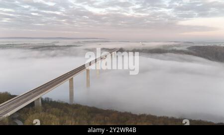 Une vue aérienne époustouflante d'un pont s'étendant sur un paysage brumeux avec un ciel nuageux Banque D'Images
