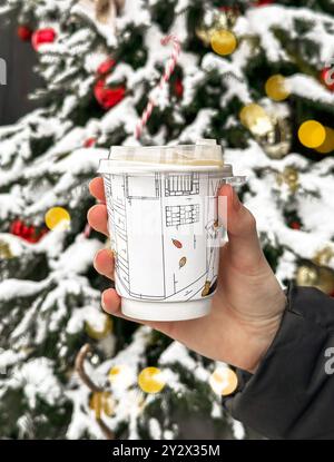 Gobelet à emporter de Noël avec couvercle pour les boissons chaudes d'hiver. Mug en papier jetable festif dans un cadre urbain enneigé, parfait pour déguster des boissons de saison Banque D'Images