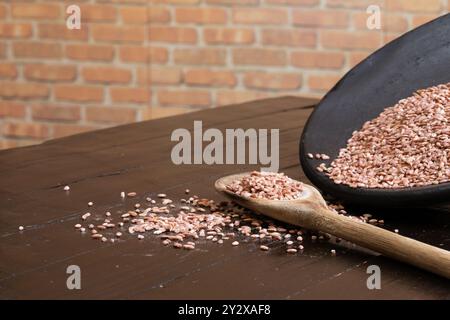 Une cuillère en bois avec du riz en terre couché sur la table à côté d'un bol en argile incliné qui a également du riz. Banque D'Images