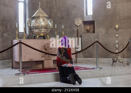 Une vieille femme s'agenouille dans l'église, devant un grand brûleur d'encens et des bougies Banque D'Images