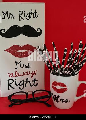 Objets décoratifs comprenant un panneau Mr. Right et Mrs Always Right, une tasse avec des pailles et des lunettes sur fond rouge. Banque D'Images