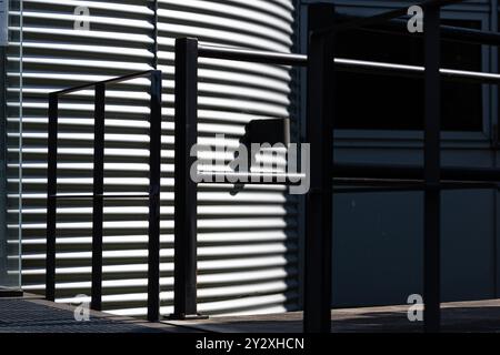 Gros plan d'une façade ondulée et d'une balustrade, baignée de soleil, forment un motif graphique. Banque D'Images