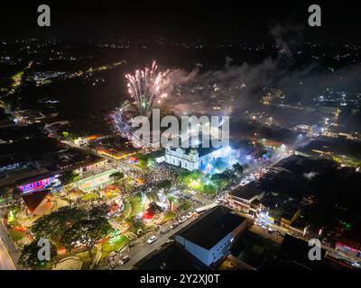 Vue aérienne d'un paysage urbain nocturne festif avec des feux d'artifice, des bâtiments illuminés et un grand rassemblement de gens dans la ville de Barva Banque D'Images