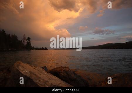 Un beau coucher de soleil sur un lac calme avec un ciel spectaculaire et un rivage rocheux. Banque D'Images