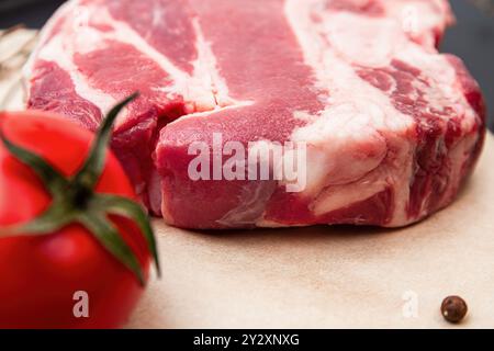 Steak de bœuf marbré cru placé à côté d'une tomate mûre, prêt pour une délicieuse préparation de repas Banque D'Images