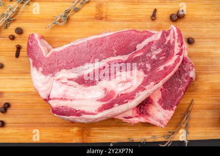 Un gros steaks de bœuf cru avec de la graisse marbrée reposant sur une planche à découper en bois, prêt à griller ou à cuire Banque D'Images